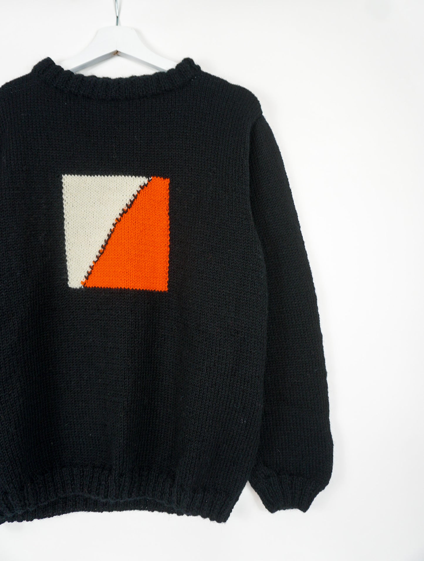 A black medium jumper with orange beige square pattern on it.