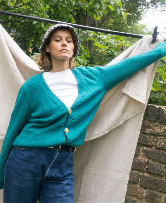 Green hand knitted cardigan with hand made buttons from recycled skateboard, wearing this a model posing, one off and from a London brand