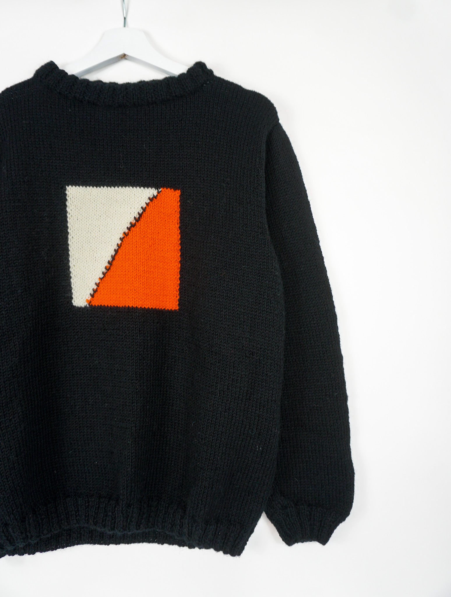 A black medium jumper with orange beige square pattern on it. 