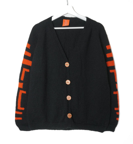Black cardigan with orange patterns on sleeves, hanging on a white background