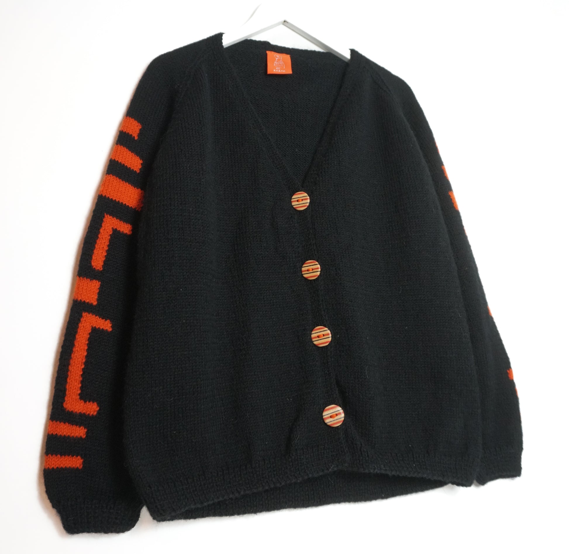 Black cardigan with orange buttons and sleeves on a white background