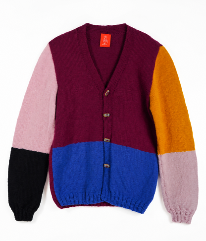 A color-block knit cardigan sweater with a burgundy body, a light pink sleeve, a mustard yellow sleeve, a blue lower body panel, and a black cuff, shown on a plain white background.