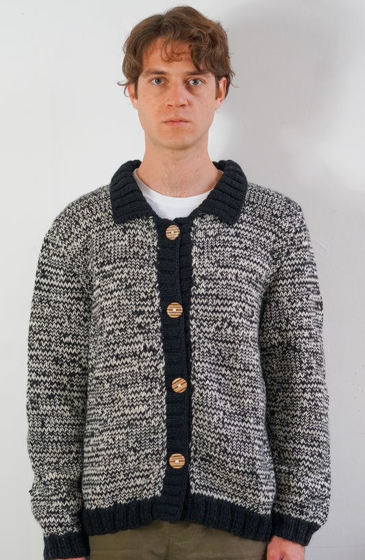 A man wearing a black and white marled knit cardigan with a dark ribbed collar, cuffs, and hem, featuring four wooden buttons down the front.