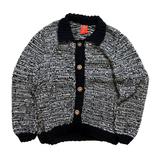 A black and white marled knit cardigan sweater with a solid black ribbed collar, button placket, and hem, featuring brown buttons, shown flat on a white background.
