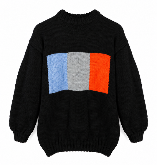 Black hand-knitted sweater with a ribbed crew neck and a geometric chest panel in pale blue, light grey and bright orange, displayed against a white background.