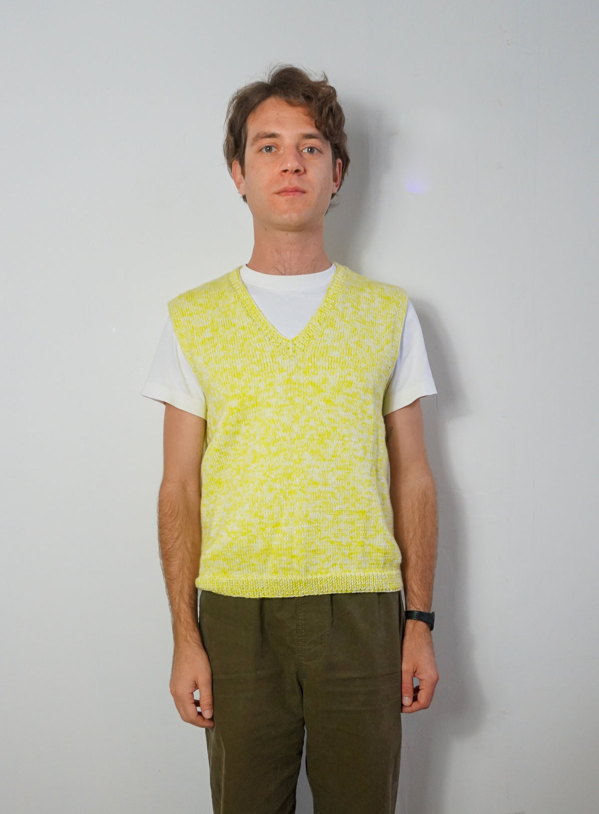 A sleeveless knit V-neck sweater vest in a bright yellow and white marled pattern, hanging on a white wooden hanger against a plain white background.